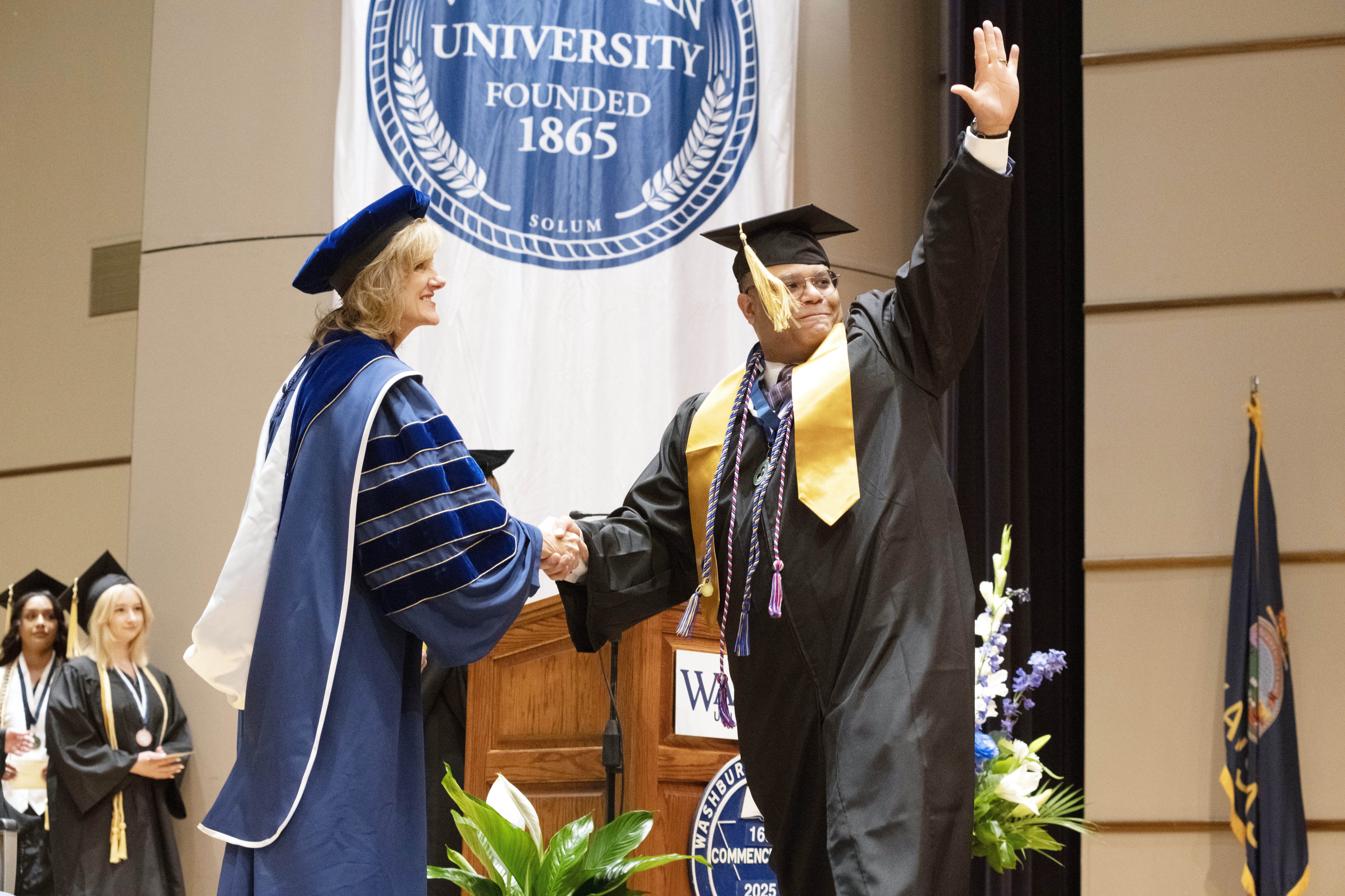 An emotional graduate shakes hands with President Mazachek and waves to the crowd as they walk across the stage.