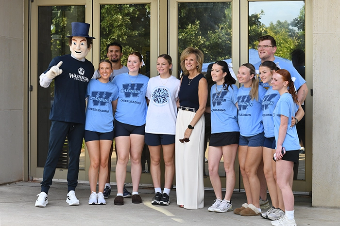 President JuliAnn Mazachek stands with Washburn cheerleaders and the Ichabod mascot outside a campus building during an event.