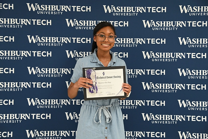 NTHS inductee poses with certificate in front of blue and white Washburn Tech backdrop.