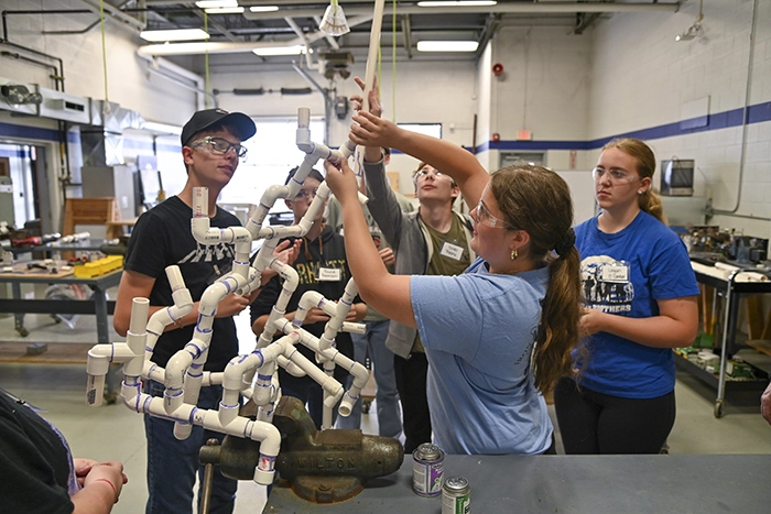 Students collaboratively assembling a complex PVC pipe structure in a workshop setting.