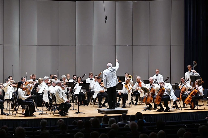 The Sunflower Music Festival Orchestra performs on stage in White Concert Hall at Washburn University as a conductor leads musicians playing strings before a seated audience.